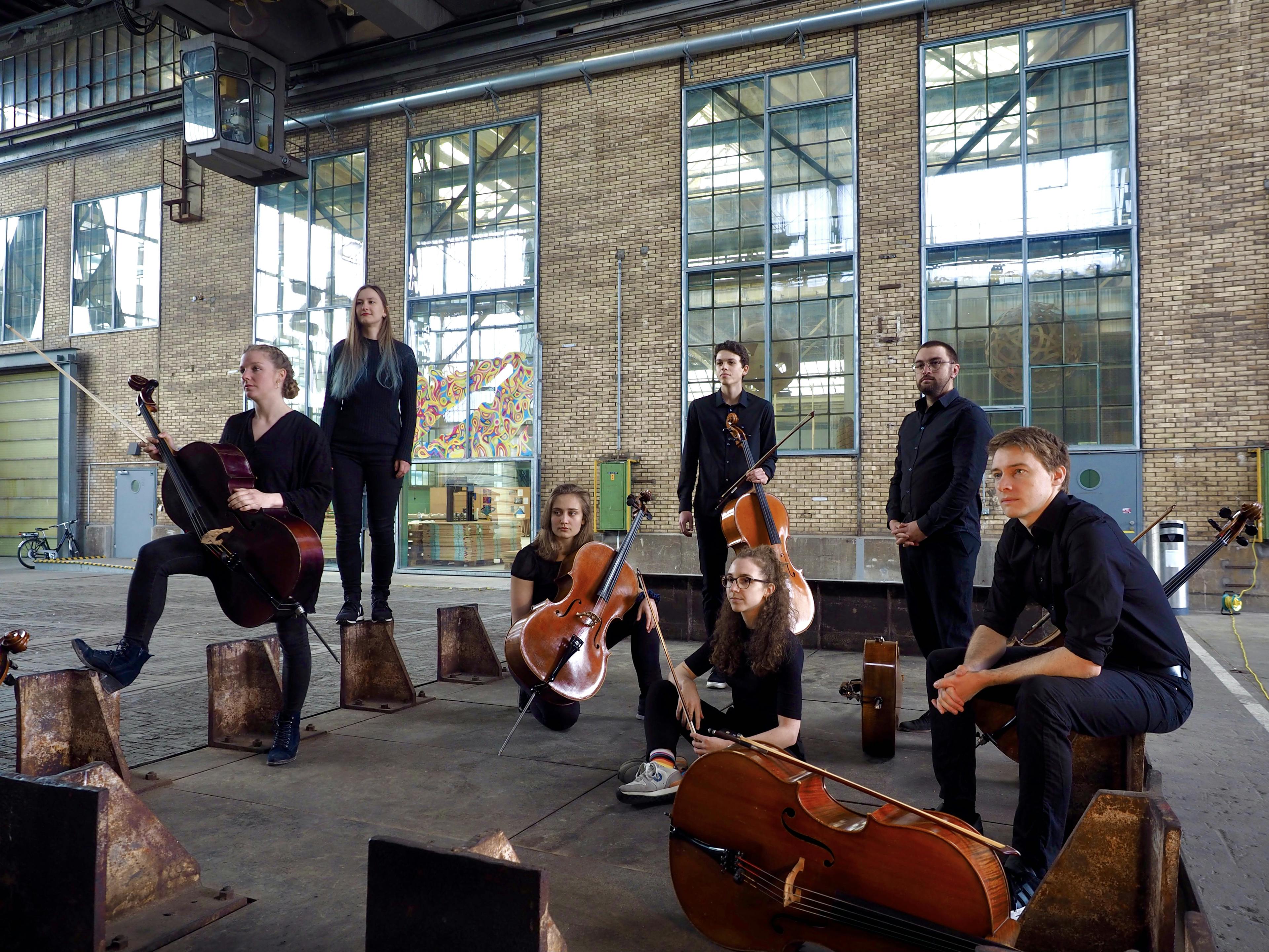 Crescelli Bandfoto; sechs schwarz gekleidete Menschen mit Cello sitzen in einer Industriehalle